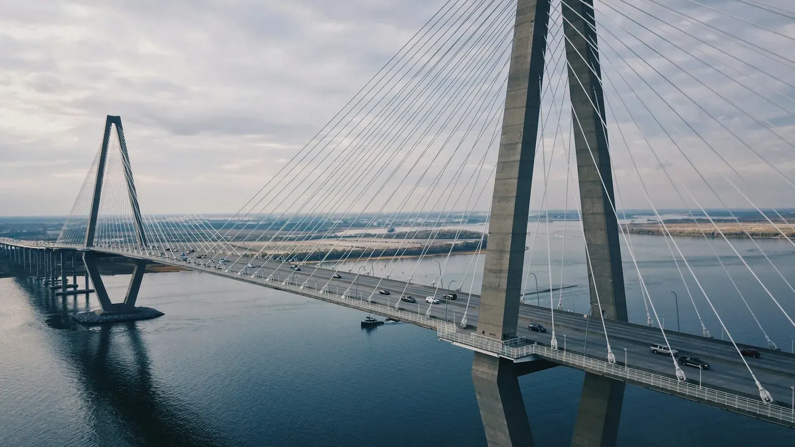 A cable-stayed suspension bridge crossing a wide river, seen from above with cars crossing the deck