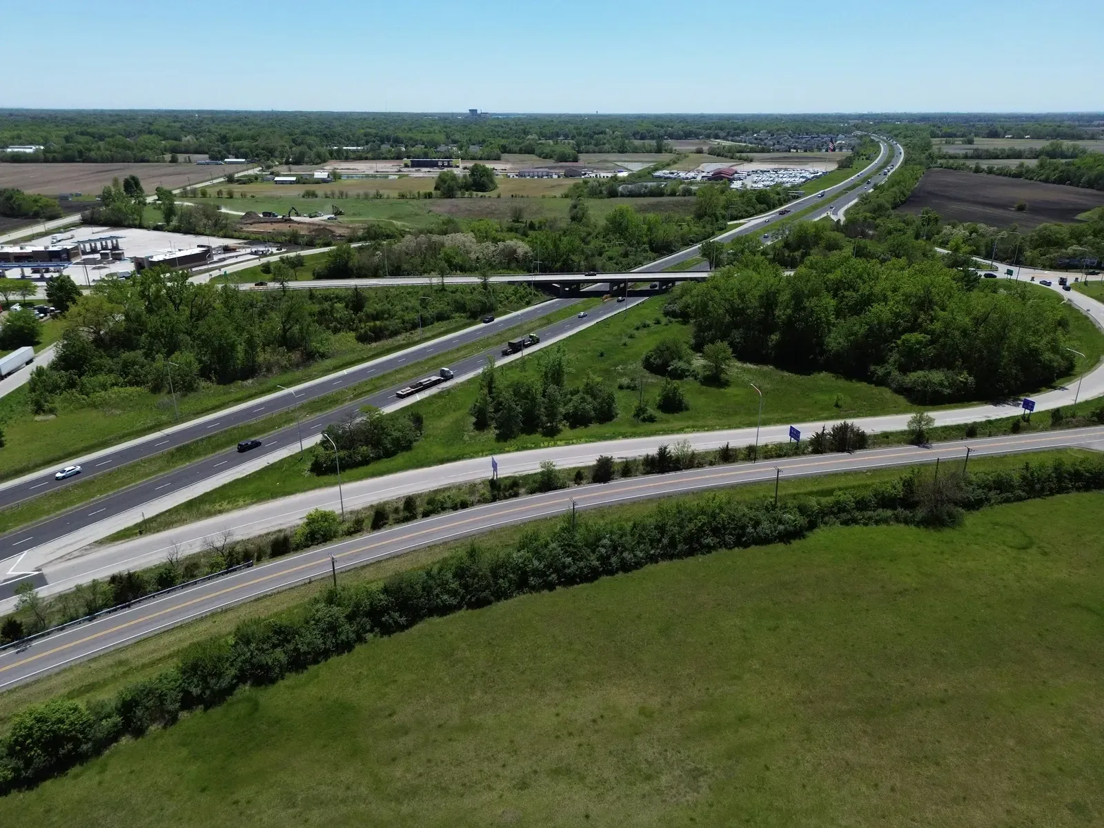 An aerial view of a rural interstate interchange with an overpass, farmland, and a truck stop below