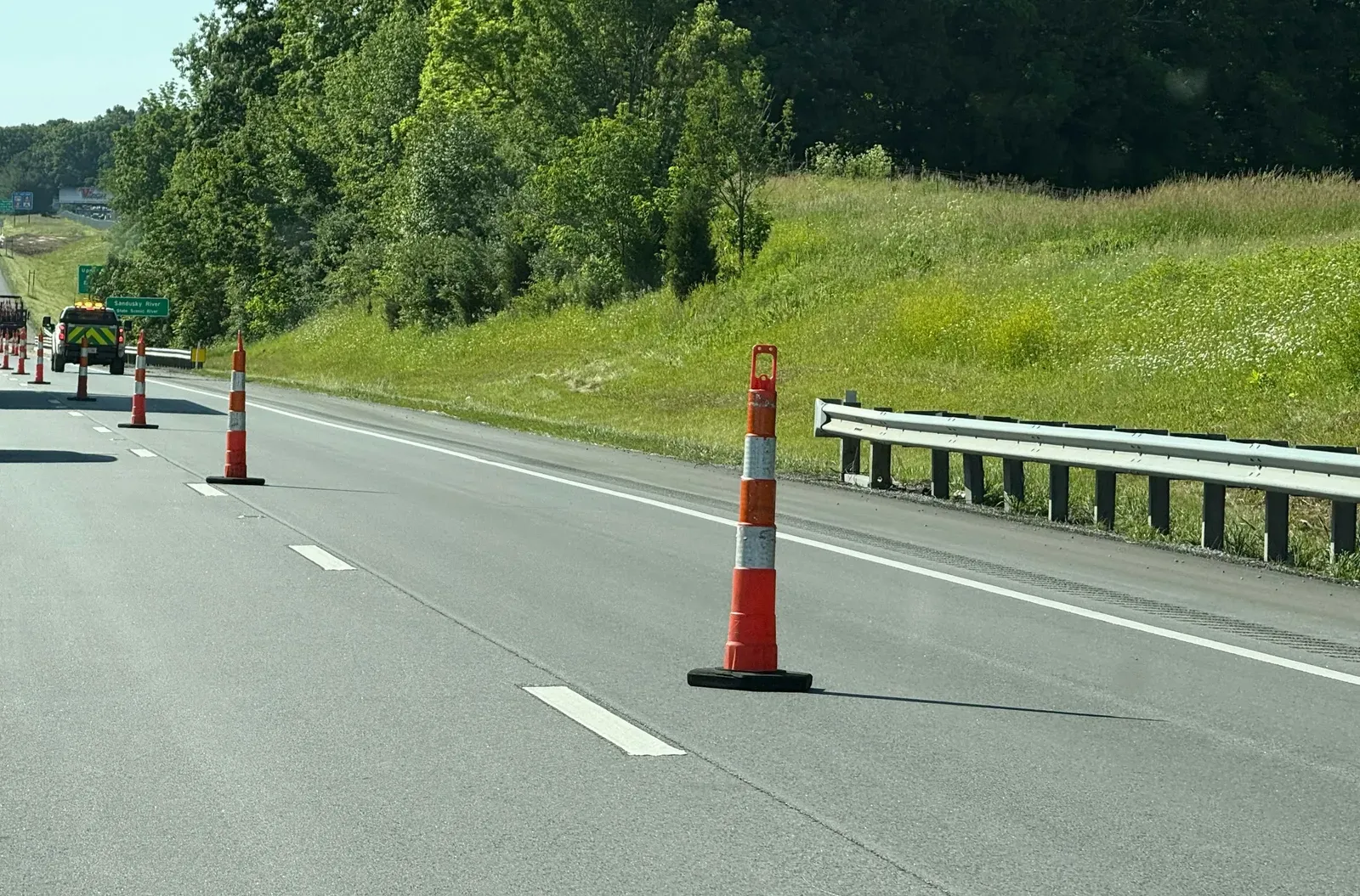 Orange traffic cones lining a highway work zone shoulder next to a guardrail and a maintenance truck