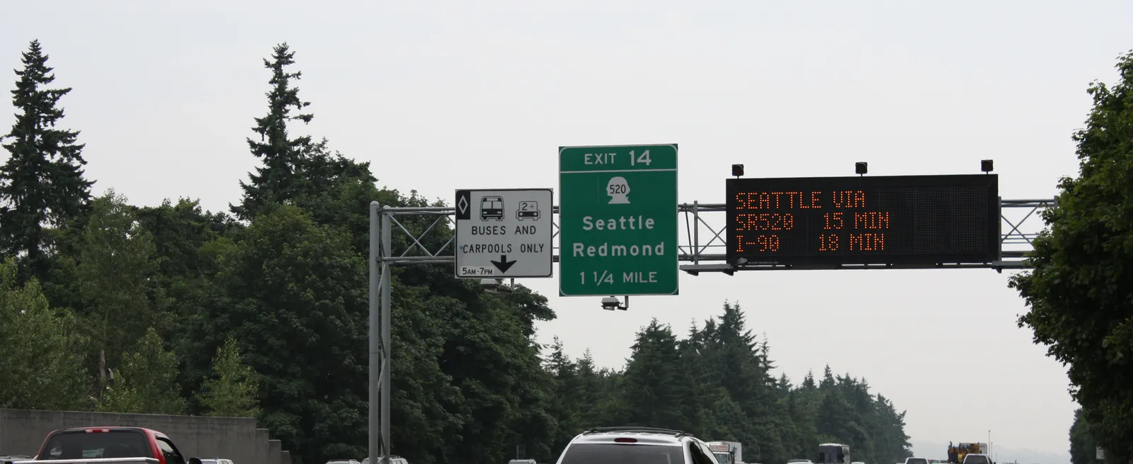Overhead gantry on I-405 in Washington with a dynamic message sign showing live travel times to Seattle beside static exit signage